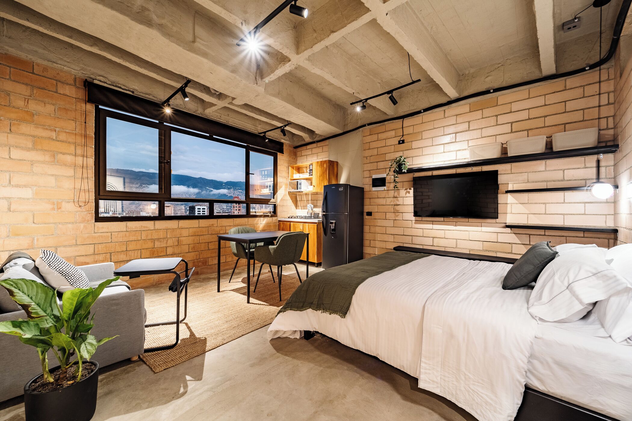 A modern bedroom with a large bed, a desk, a chair, and a TV mounted on the wall.