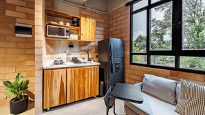 Eine kleine Küche mit Holzausstattung, einer integrierten Mikrowelle und einem Kühlschrank. Ein Fenster bietet Blick auf Bäume, und es gibt eine kleine Sitzecke mit Kissen.