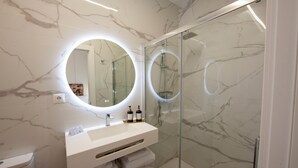 A modern bathroom with a marble vanity, a round mirror, and a glass-enclosed shower. - Pries Homes - La casa azul (Málaga)
