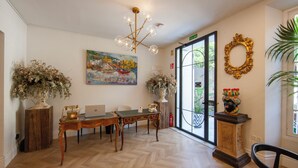 A room with a wooden herringbone floor, a wooden table with chairs, a painting on the wall, a chandelier, and a large window with a view of greenery. - Pries Homes - La casa azul (Málaga)