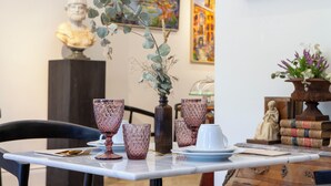 A dining table set with pink glassware, a vase with dried plants, and a bust sculpture in the background. - Pries Homes - La casa azul (Málaga)