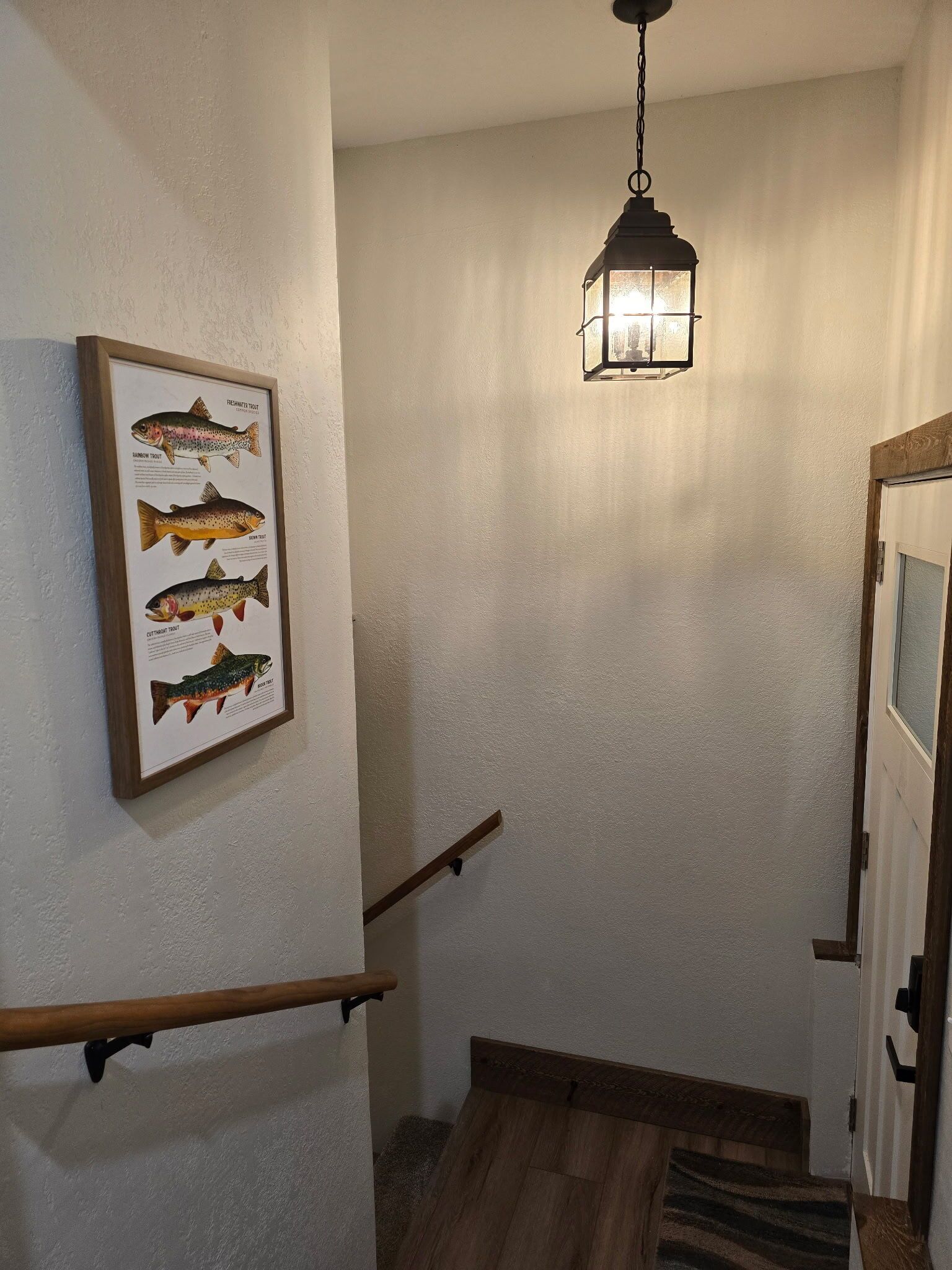 Una scala con corrimano in legno, un quadro con un'illustrazione di un pesce sulla parete e un lampadario appeso.