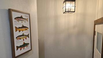 Una scala con corrimano in legno, un quadro con un'illustrazione di un pesce sulla parete e un lampadario appeso.