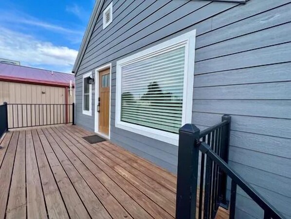Um deck de madeira com guarda-corpo de metal, uma porta de garagem e uma janela com persianas.