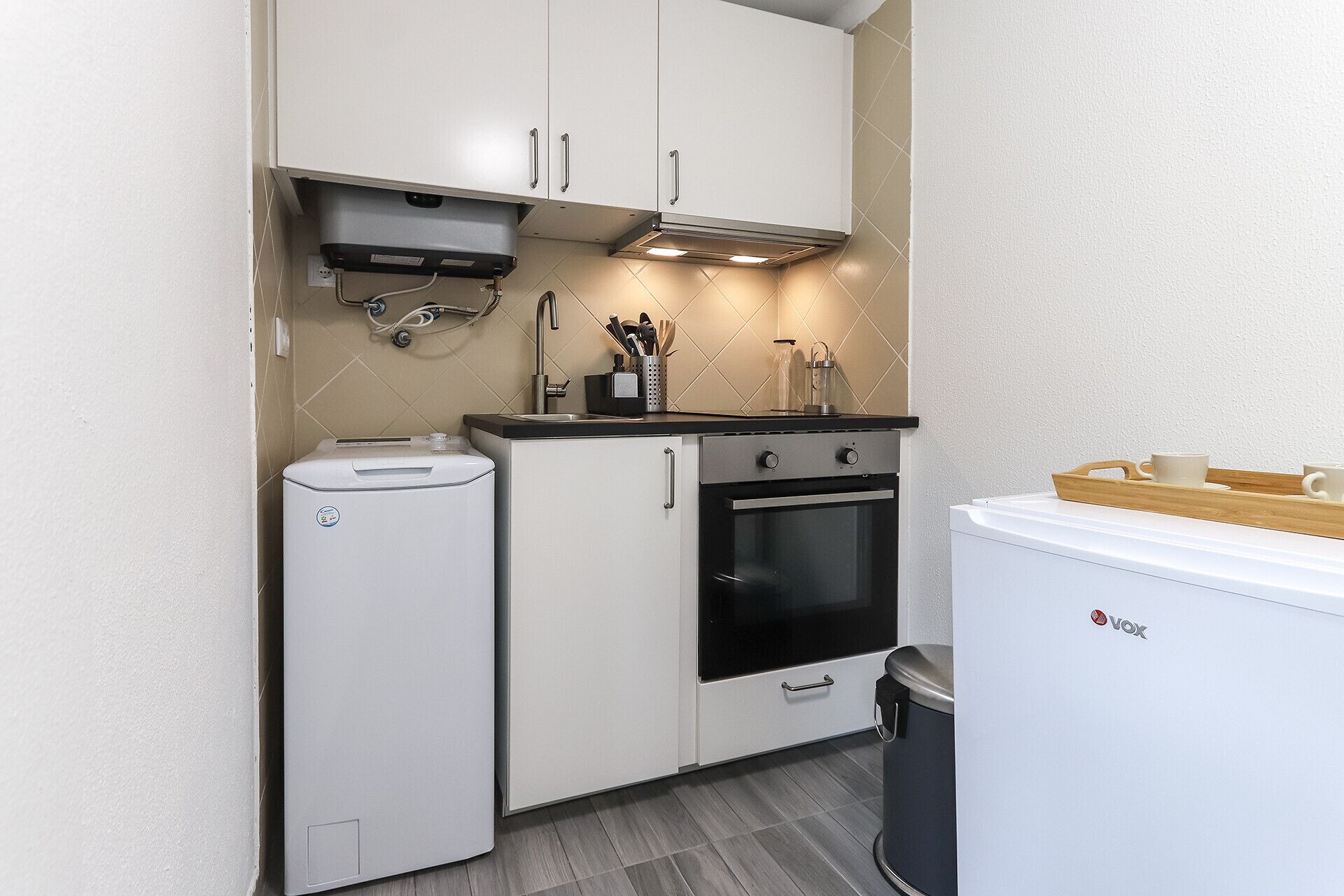 A compact kitchen with white cabinets, a built-in oven, a dishwasher, and a small refrigerator.