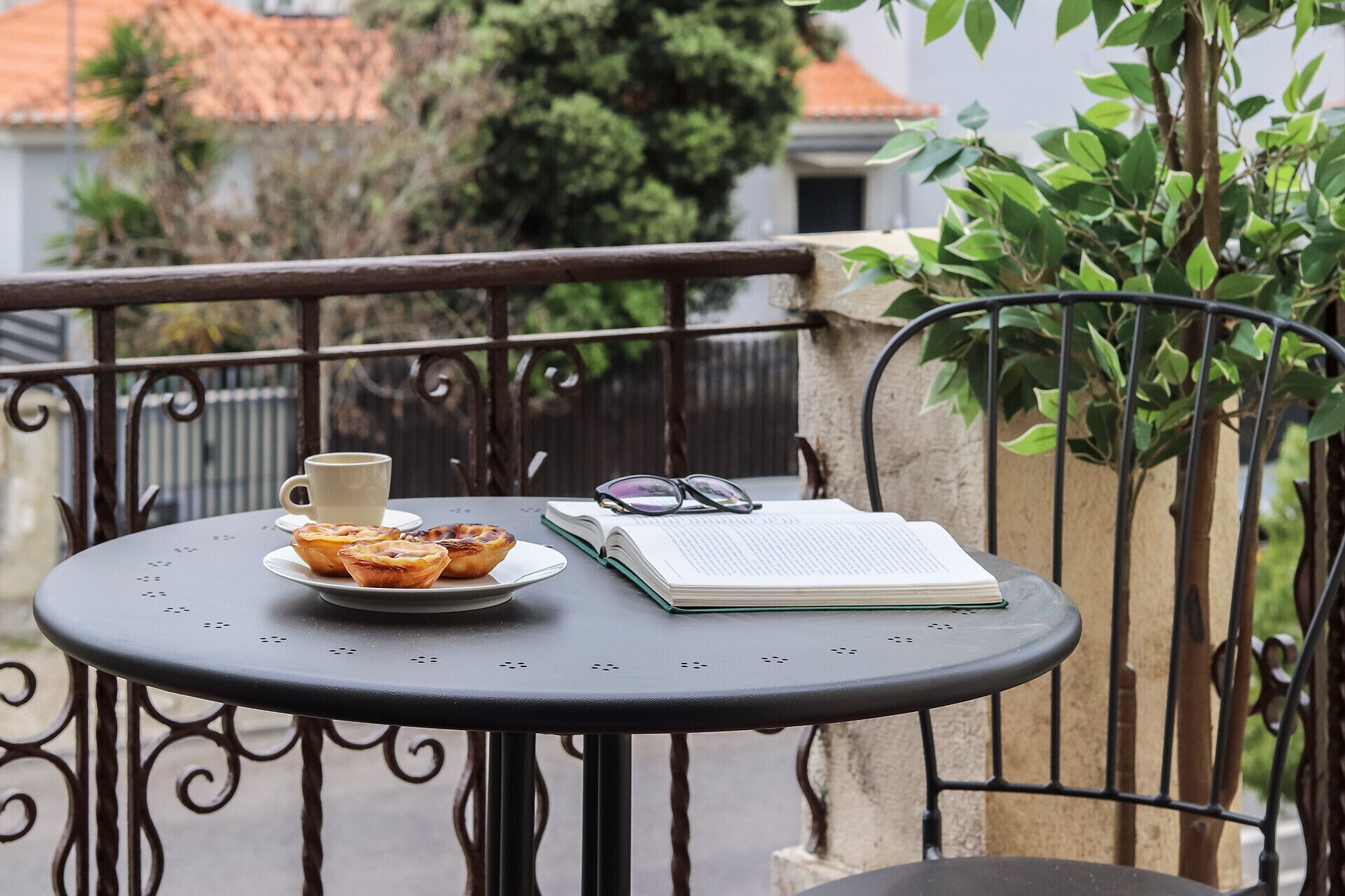 A round table with a cup, pastries, and an open book on a balcony.