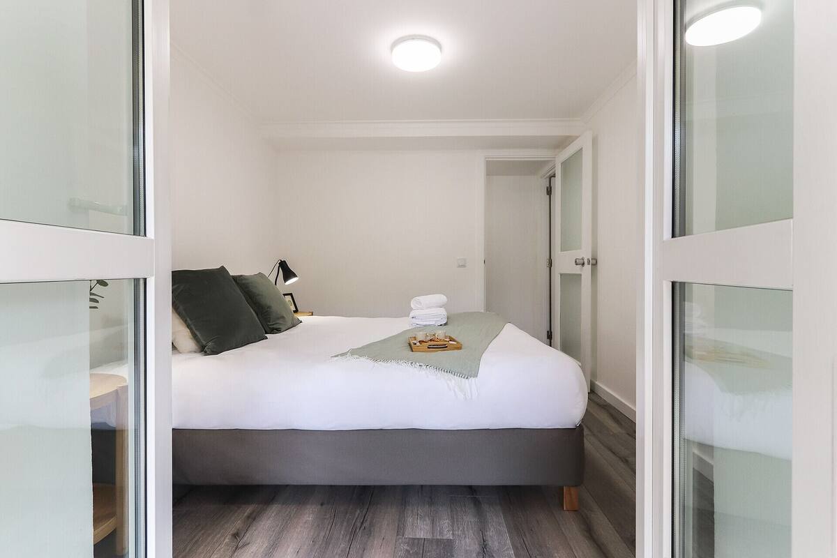 Una camera da letto con un letto, una lampada da comodino, un vassoio con oggetti e una porta che dà su un'altra stanza.
