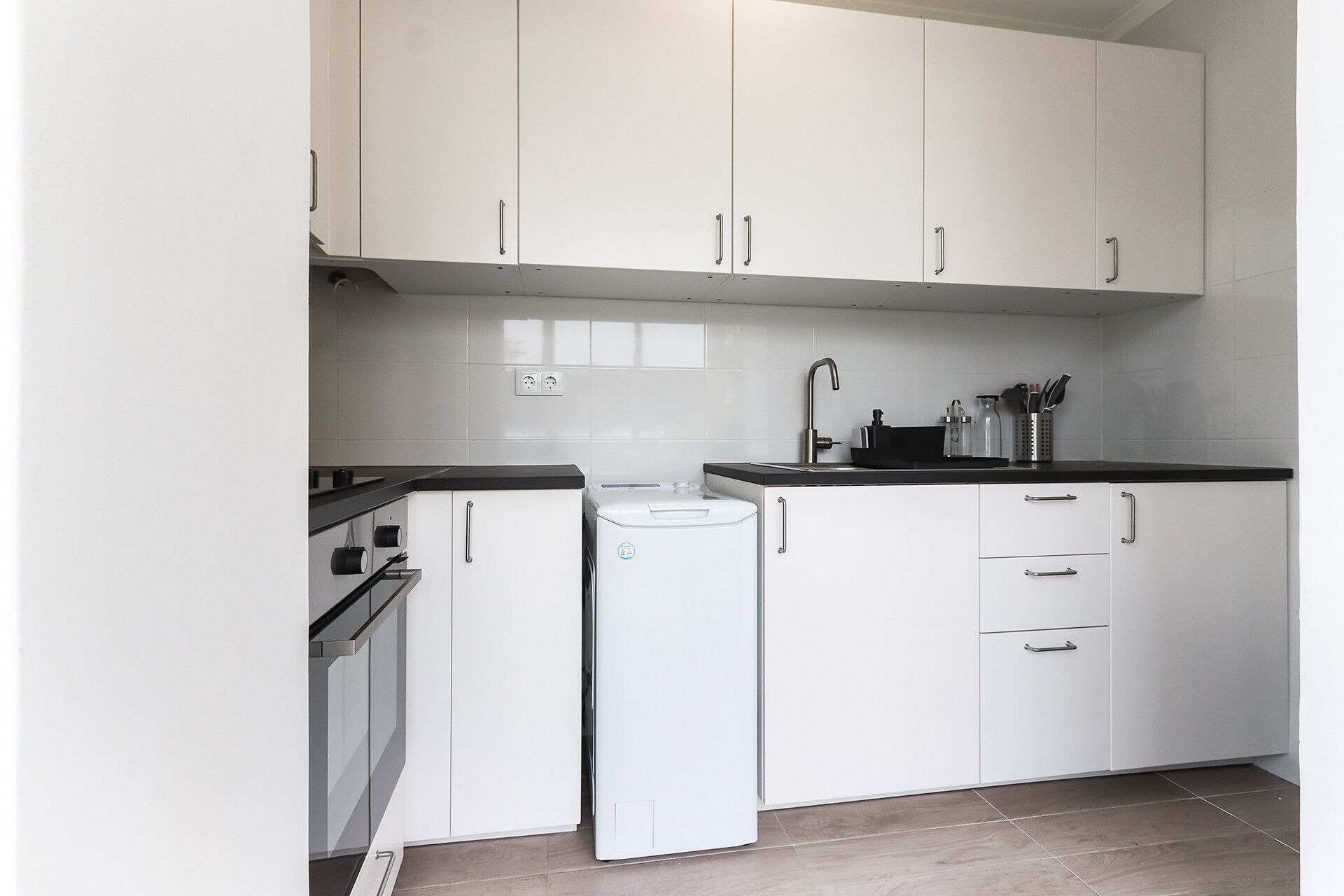 Una cocina moderna con armarios blancos, encimera negra y horno integrado.