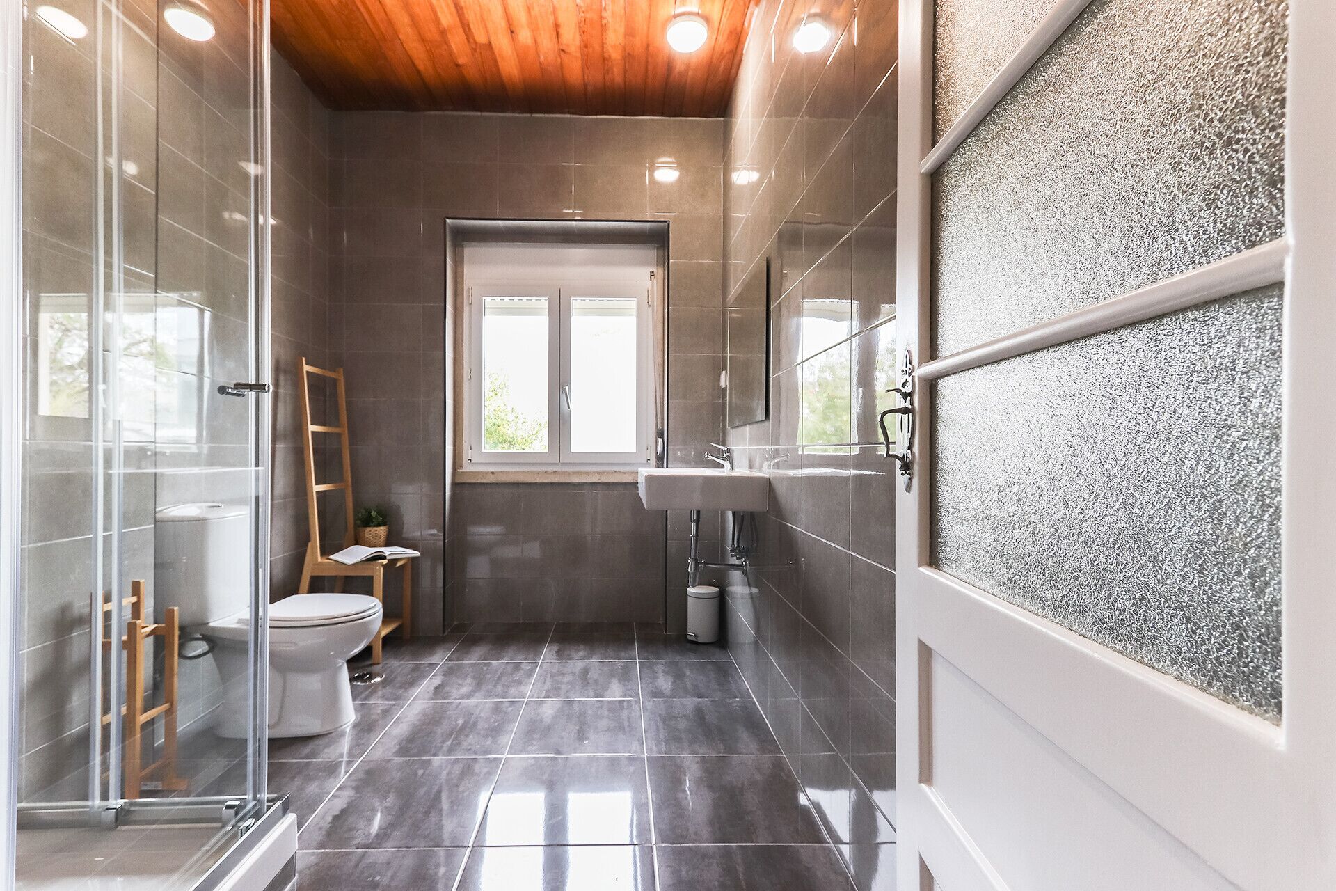 A modern bathroom with a glass shower enclosure, a white toilet, and a sink under a window.