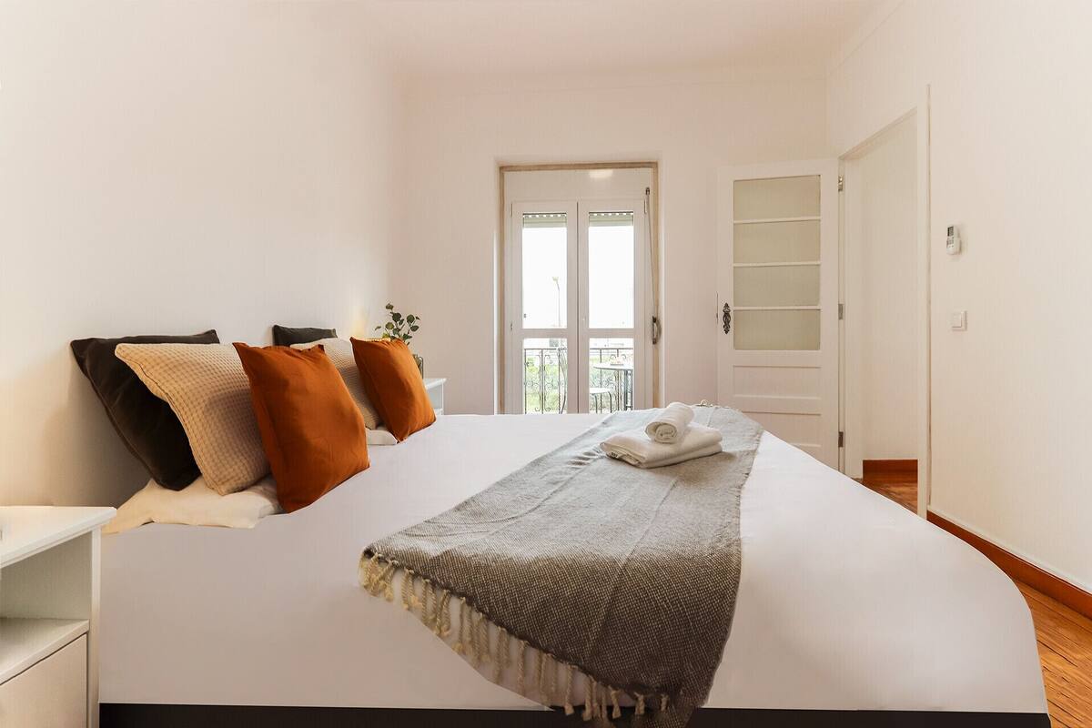 Una camera da letto con un letto, cuscini, una coperta e una porta che dà su un balcone.