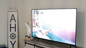 Ein Wohnzimmer mit Flachbildfernseher auf einer weißen Kommode, einer Wanddekoration und einem Holzschild.