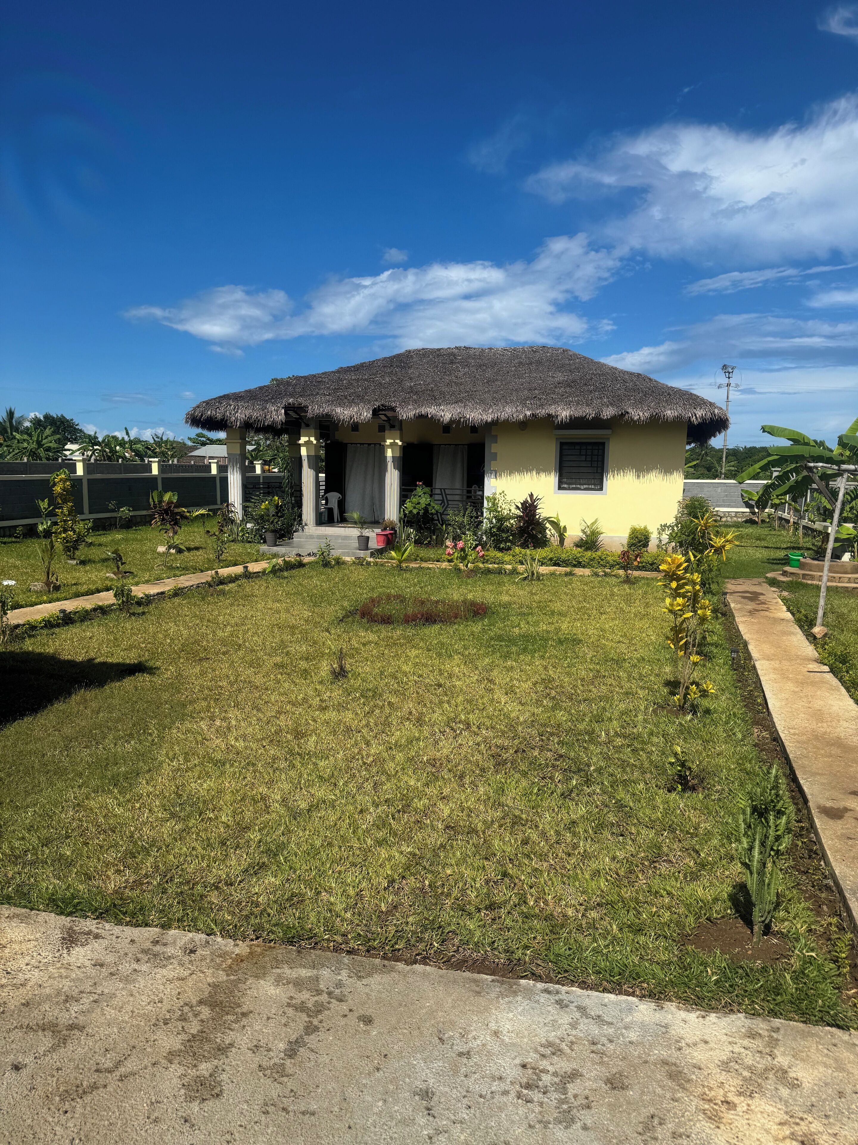 Uma casa térrea com telhado de colmo, um pequeno alpendre e um gramado bem cuidado.
