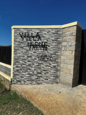 A sign for Villa Irene with a stone facade and a black gate in the background. - CHARMING VILLA WITH GARDEN AND STAFF NEAR THE BEACHES; LONG-TERM RENTAL AVAILABLE. (nosy be)