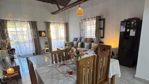 A dining area with a table set for four, wooden chairs, a ceiling fan, and a refrigerator. - CHARMING VILLA WITH GARDEN AND HOUSE STAFF IN NOSY BÉ, CLOSE TO THE BEACHES (nosy be)