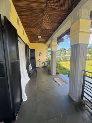 A covered outdoor area with a tiled floor, a ceiling with a geometric pattern, and a view of a green landscape. - CHARMING VILLA WITH GARDEN AND HOUSE STAFF IN NOSY BÉ, CLOSE TO THE BEACHES (nosy be)