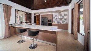 Una cucina moderna con isola centrale, due sgabelli da bar, soffitto in legno e vista esterna.