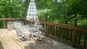 Um deck de madeira com uma mesa redonda e cadeiras, um guarda-sol e uma banheira de hidromassagem.