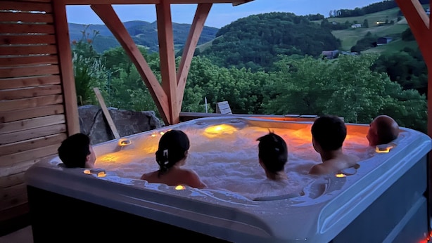 A hot tub with four people, surrounded by wooden beams and a view of a green landscape. - Luxury Chalet with Sauna and Hot Tub (Fréland)