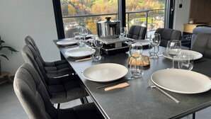 A dining table set for six with a scenic view of autumn foliage through large windows. - Luxury Chalet with Sauna and Hot Tub (Fréland)