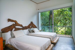A room with two beds, a large wooden headboard, and a sliding glass door leading to a balcony with a view of trees. - Casa Bromelia (Savegre)