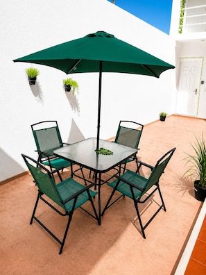 Eine Terrasse mit Tisch, Stühlen, Sonnenschirm und Kübelpflanzen.