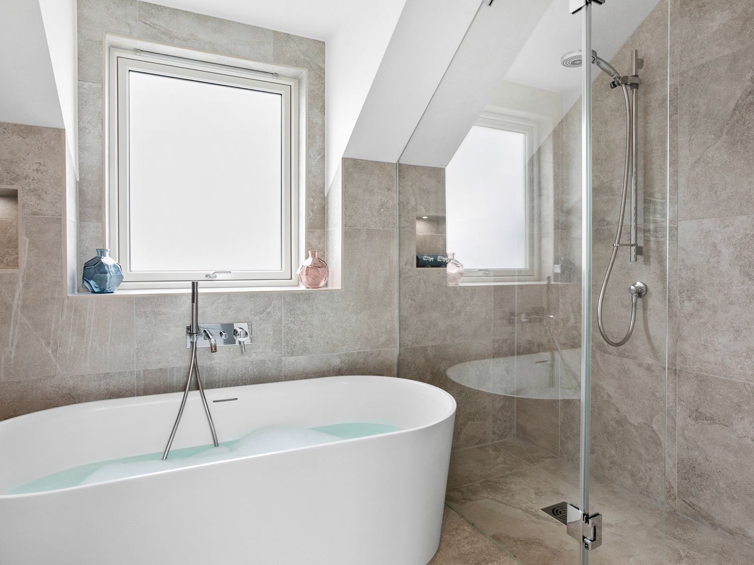 Een moderne badkamer met een vrijstaand bad, een douche met glazen wanden en een groot raam boven het bad.
