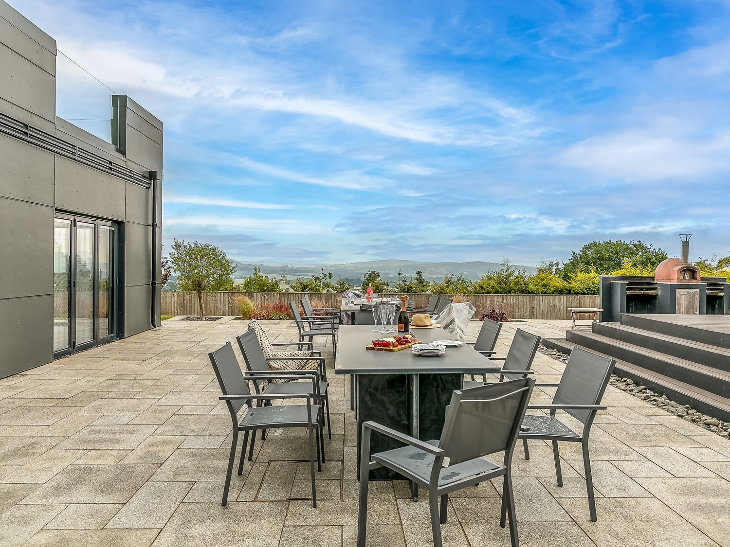 An outdoor patio with a table set for dining, surrounded by chairs, and a pizza oven.