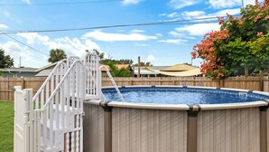 An above-ground swimming pool with a white safety gate and ladder, surrounded by a wooden fence and a tree with pink flowers. - Private Pool & Grill ~ 8 Min to Beach ~ Pets Welcome ~ Near Clearwater Beach (Largo)