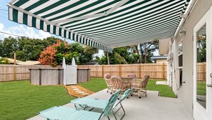A patio with a striped awning, a table and chairs, a grill, and a wooden fence. - Private Pool & Grill ~ 8 Min to Beach ~ Pets Welcome ~ Near Clearwater Beach (Largo)