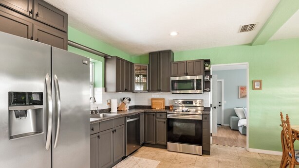 A modern kitchen with stainless steel appliances, dark cabinets, and a green accent wall. - Private Pool & Grill ~ 8 Min to Beach ~ Pets Welcome ~ Near Clearwater Beach (Largo)