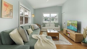 A living room with a green sofa, white cushions, a white throw blanket, a coffee table, a TV on a wooden stand, and a ceiling fan. - Private Pool & Grill ~ 8 Min to Beach ~ Pets Welcome ~ Near Clearwater Beach (Largo)