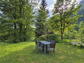 An outdoor dining area with a table and chairs surrounded by lush greenery and trees. - Assy's Cocoon (Passy)