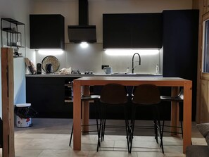 A modern kitchen with a central island, black cabinets, and a wooden dining table with four chairs. - Assy's Cocoon (Passy)