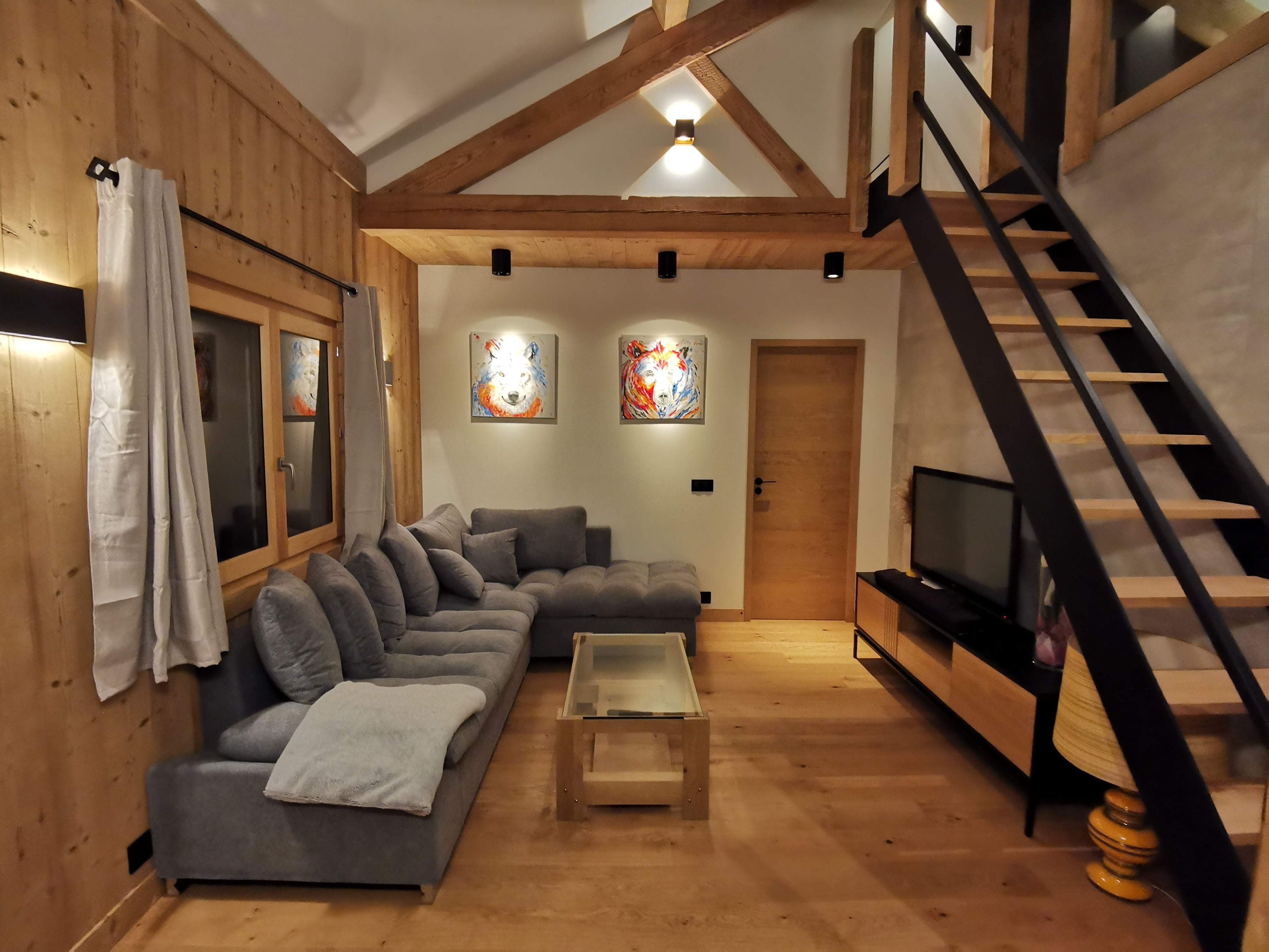 A modern living room with a sectional sofa, a coffee table, a TV, and a staircase.