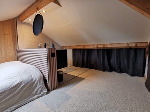 A bedroom with a bed, a small table, a hanging light fixture, and a window with curtains. - Assy's Cocoon (Passy)