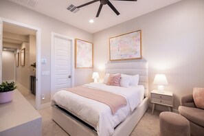 Un dormitorio con cama, mesitas de noche, ventilador de techo y obras de arte en las paredes.