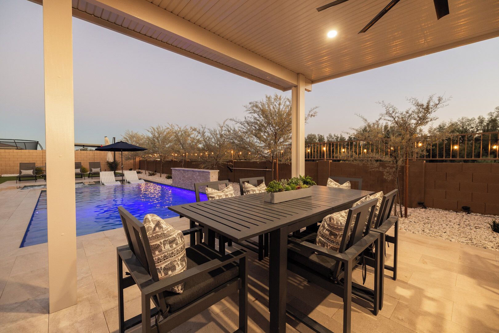 A covered outdoor area with a pool, a dining table with chairs, and a barbecue grill.