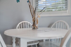 A round white table with two white chairs, a vase with branches, and a window with blinds.