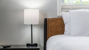 Un lit avec du linge de lit blanc, une table de chevet noire avec une télécommande, et une lampe avec un abat-jour blanc.