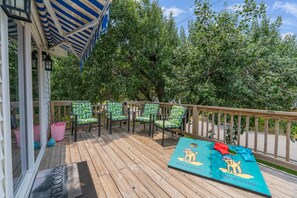 A wooden deck with four green chairs, a welcome mat, and a blue mat with a dog illustration.