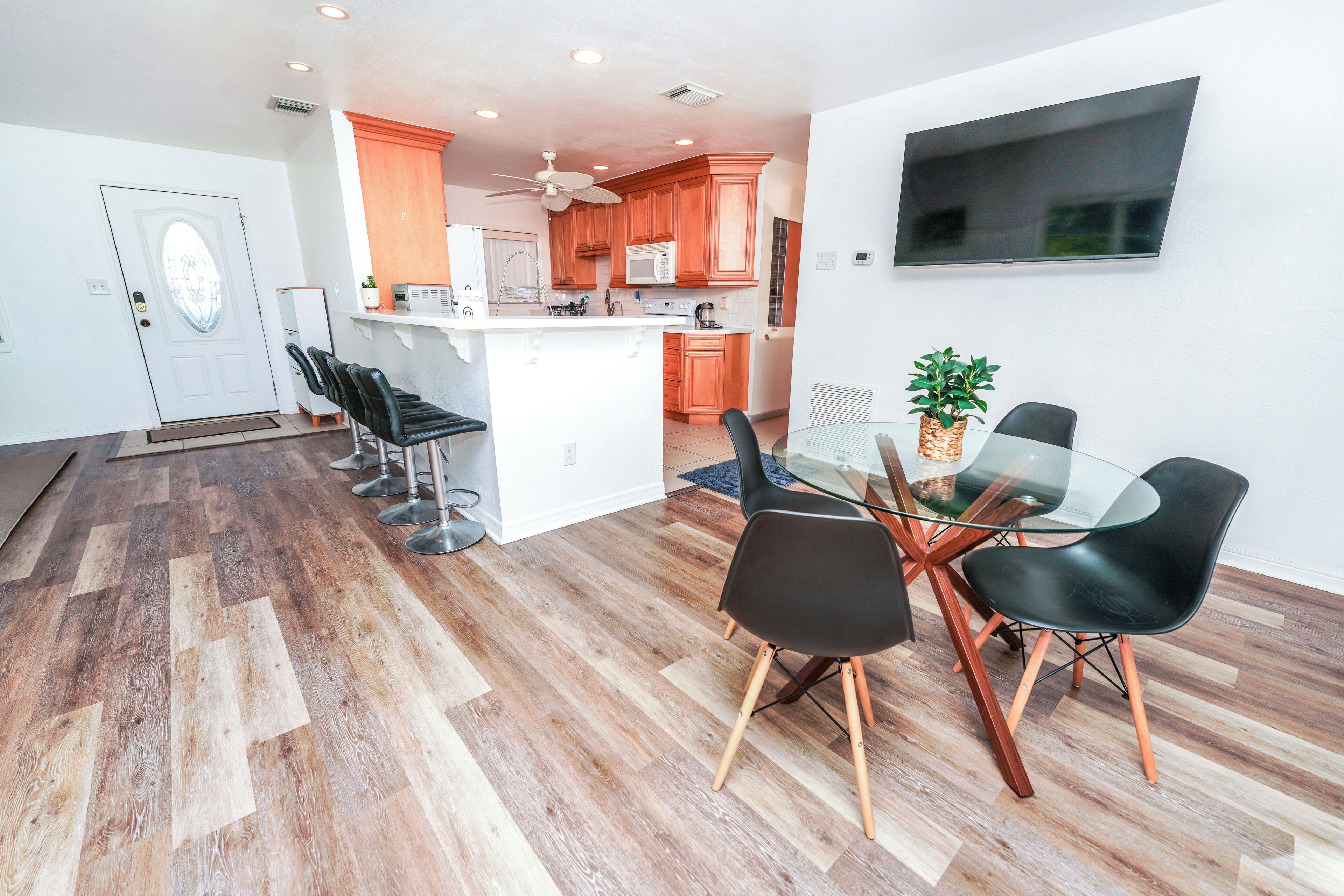 A modern kitchen with wooden cabinets, a microwave, and a ceiling fan. There is a dining area with a glass table and black chairs.