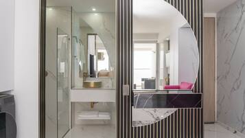 A modern bathroom with a glass partition, a vanity with a gold sink, and a large mirror.