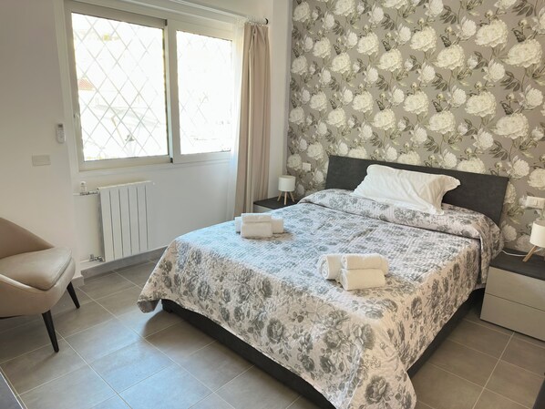 A neatly arranged bedroom with a bed, a chair, and a nightstand.