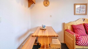 Ein Bett aus Holz mit herzenmusterten Kissen, ein Holztisch mit einer Uhr und ein gerahmtes Bild an der Wand.