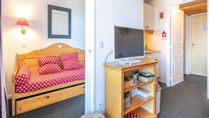 Ein gemütliches Zimmer mit einem Holzbett, einem Fernseher auf einem Holzschrank und einer kleinen Küchenzeile.