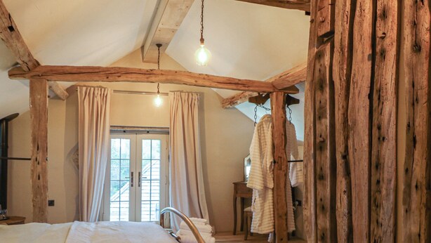 Un dormitorio rústico con una cama grande, vigas de madera, una lámpara colgante y vistas al exterior a través de una ventana.
