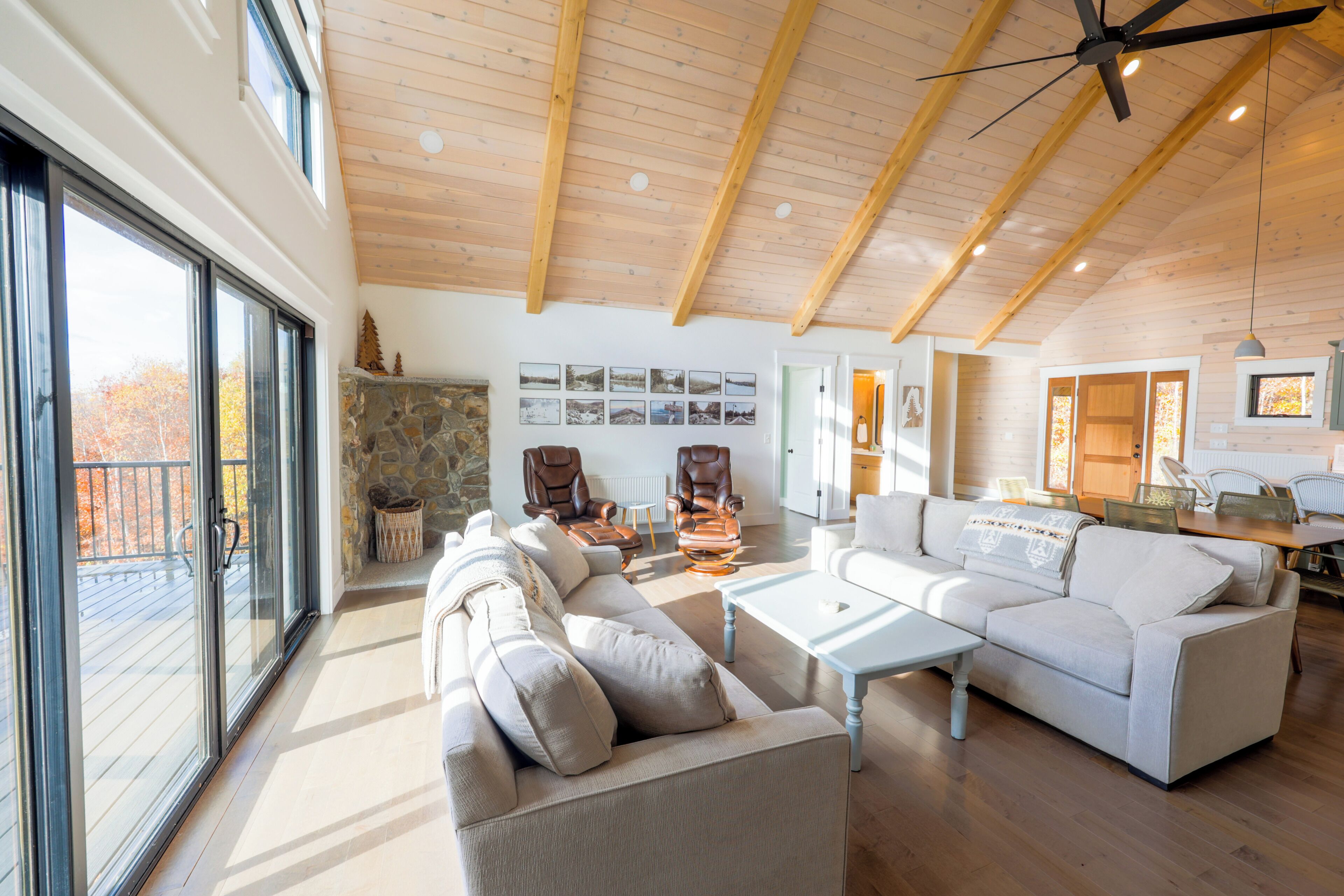 A spacious living room with a high ceiling, large windows, and a stone fireplace.