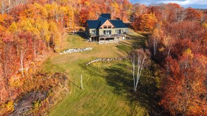 A large house with a dark roof, surrounded by a forest with autumn foliage. - Mountain Escape - Views • Firepit • Near Sugarloaf (Kingfield)