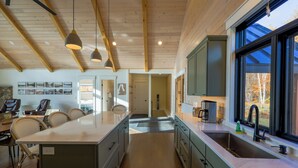 A modern kitchen with wooden beams, a large island, and a view of the outdoors. - Mountain Escape - Views • Firepit • Near Sugarloaf (Kingfield)