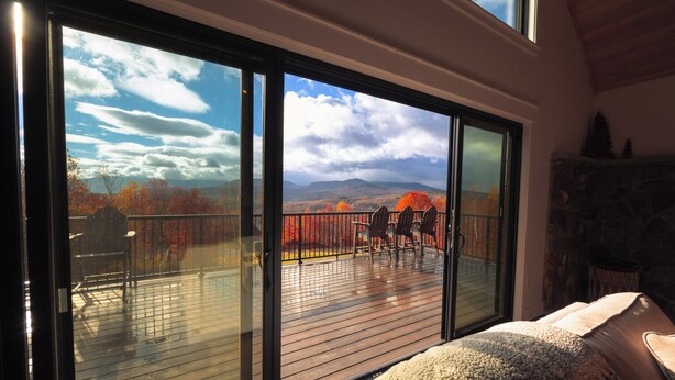 A room with a large sliding glass door leading to an outdoor deck with a view of autumn trees and mountains. - Mountain Escape - Views • Firepit • Near Sugarloaf (Kingfield)